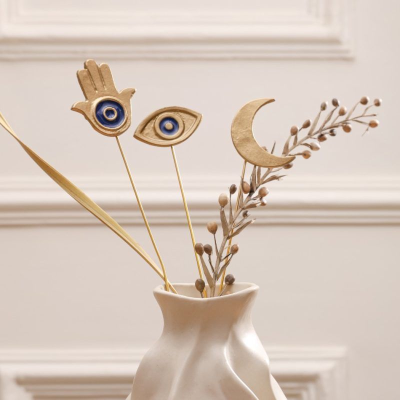 Close-up of the Golden Persian charm set (Moon, Eye, Hamsa) displayed in a modern white vase with dried botanicals.
