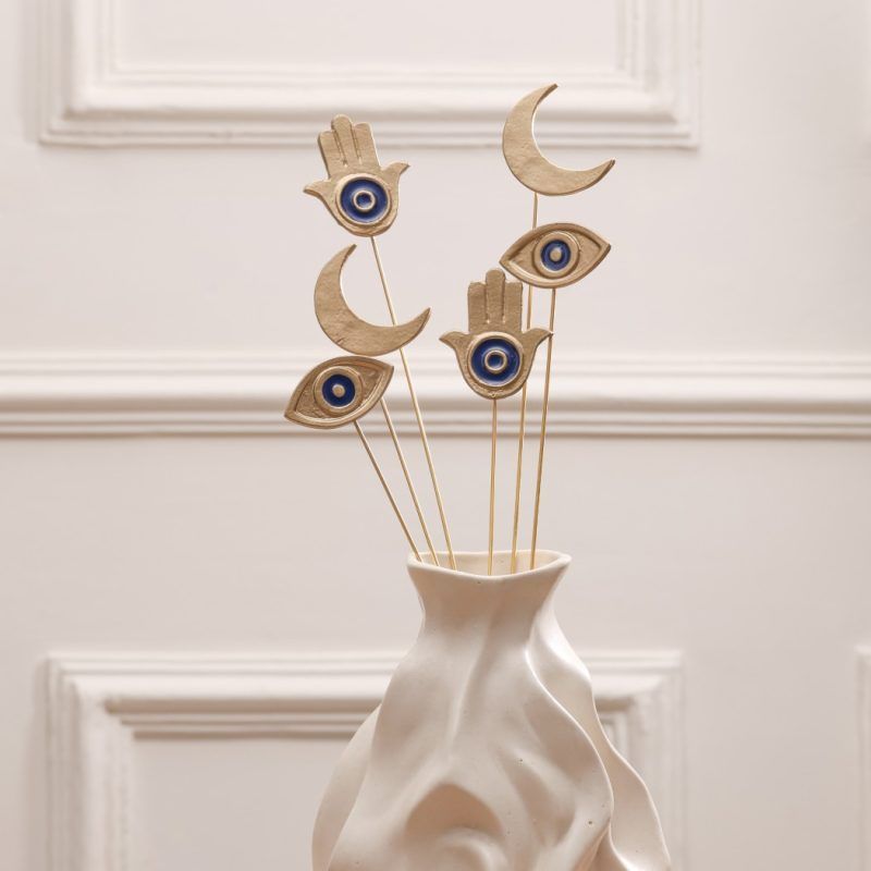 Close-up of the set of 6 golden sticks (2 Moons, 2 Hamsas, 2 Eyes) standing in a textured white vase without floral accents.