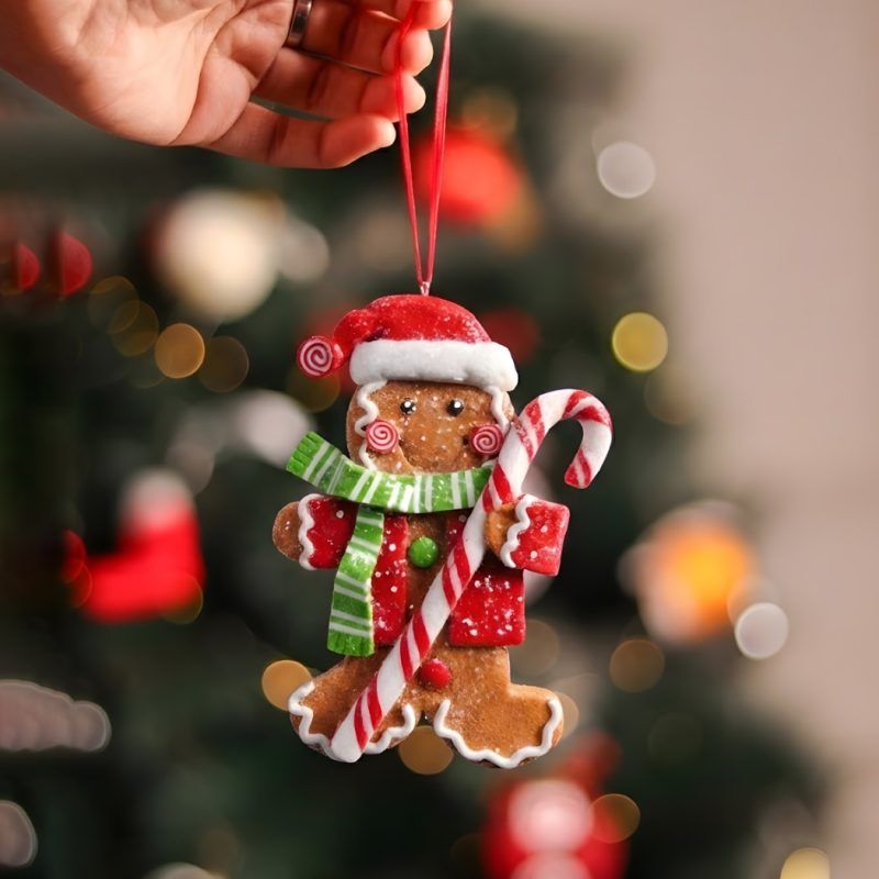 Close-up of the male figure from the Christmas tree gingerbread ornaments set of 2, wearing a Santa hat and green striped scarf held against a festive blurred background.