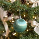 Mint green satin finish Christmas bauble hanging on a pine tree branch.