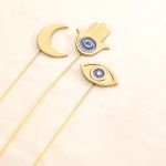 Flat lay showing the complete set of 3 golden metal vase fillers: a Crescent Moon, a Hamsa Hand, and an Evil Eye symbol.