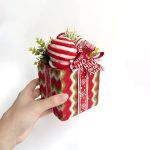 A hand holding the decorative Christmas box to demonstrate its small, handheld scale and lightweight design.
