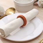 Rustic boho place setting featuring a single burnt orange knitted-style napkin ring securing a white cloth napkin.