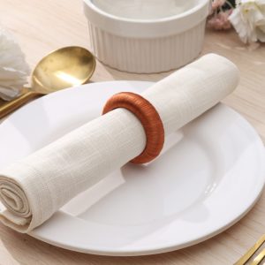 Rustic boho place setting featuring a single burnt orange knitted-style napkin ring securing a white cloth napkin.