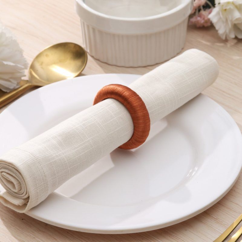 Rustic boho place setting featuring a single burnt orange knitted-style napkin ring securing a white cloth napkin.