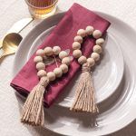 A pair of Glimpse Homes Wooden Bead Napkin Rings displayed on a plate, showcasing the flexible loop design and decorative tassels.