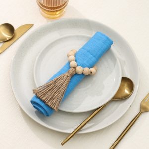 A complete boho-chic place setting featuring the Glimpse Homes Wooden Bead Napkin Ring holding a blue linen napkin.