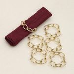 Top view of six champagne gold decorative napkin rings arranged as a set on a textured white background.