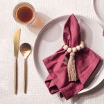 Elegant farmhouse table decor featuring a Glimpse Homes Wooden Bead Napkin Ring With Tassel on a burgundy napkin.