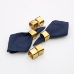 A display of Glimpse Homes Golden Cuff Napkin Rings scattered with a folded napkin to show the available set of 6.