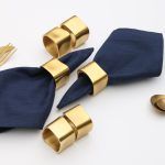 Top-down view of a set of 6 Glimpse Homes Golden Cuff Napkin Rings arranged with a navy blue napkin to showcase the matte finish.