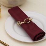 Detailed side view of a luxury champagne gold knot napkin ring holding a maroon cotton napkin.