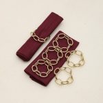 Set of six champagne gold metal knot napkin rings arranged with maroon napkins for elegant table decor.