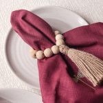 Detailed angled shot of the Glimpse Homes napkin ring showing the texture of the natural wooden beads and rustic jute tassel.