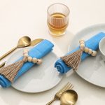 A dining arrangement for two featuring Glimpse Homes Wooden Bead Napkin Rings styled with blue napkins and modern gold flatware.