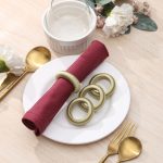 Top-down view of a dining set featuring four green thread napkin rings, styled with gold cutlery and maroon napkins.