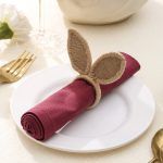 Close-up of a rustic jute bunny ear napkin ring holding a maroon napkin, ideal for Easter table settings.