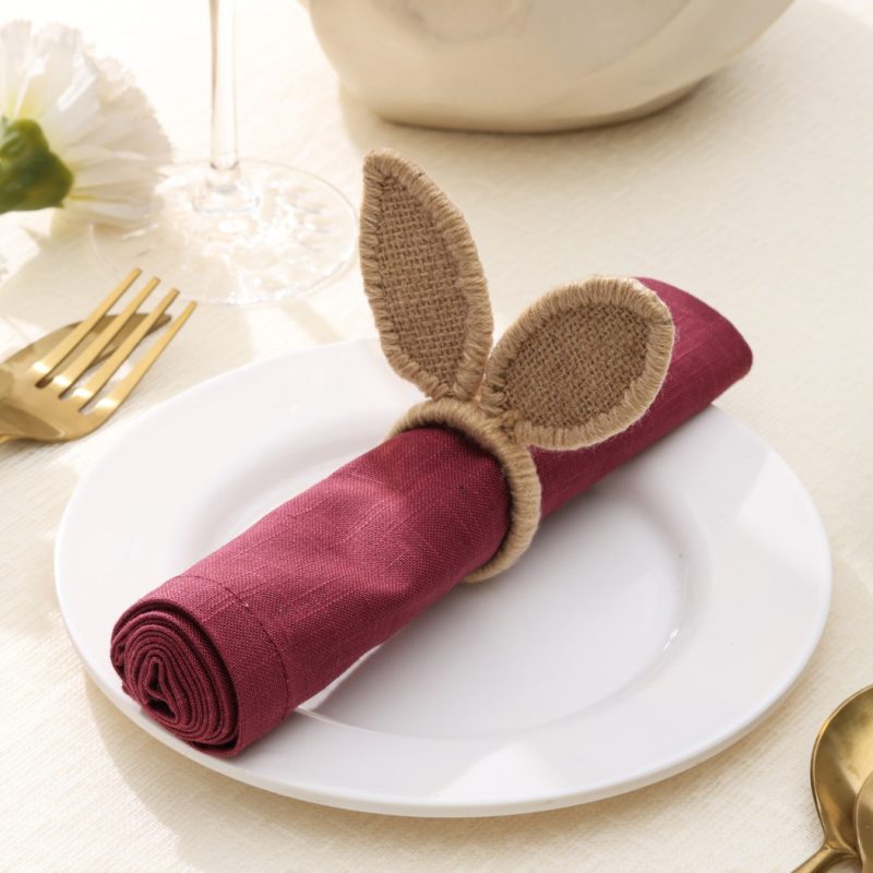 Close-up of a rustic jute bunny ear napkin ring holding a maroon napkin, ideal for Easter table settings.