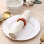 Minimalist top-down view of a white dinner plate featuring a vibrant orange yarn-wrapped napkin ring.