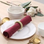 Modern dining table decor featuring a textured green yarn napkin ring on a simple white plate.