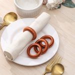 Top-down view of a dining set featuring four rust-colored thread napkin rings arranged on a white plate.