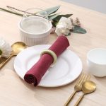Rustic chic place setting featuring a light green knitted-style napkin ring, water glass, and floral decor.