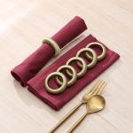 Flat lay display showing a set of six sage green yarn napkin rings arranged on folded maroon table linens.