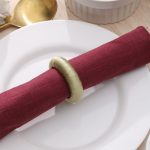 Close-up detail of a sage green yarn-wrapped napkin ring securing a burgundy linen napkin on a white plate.