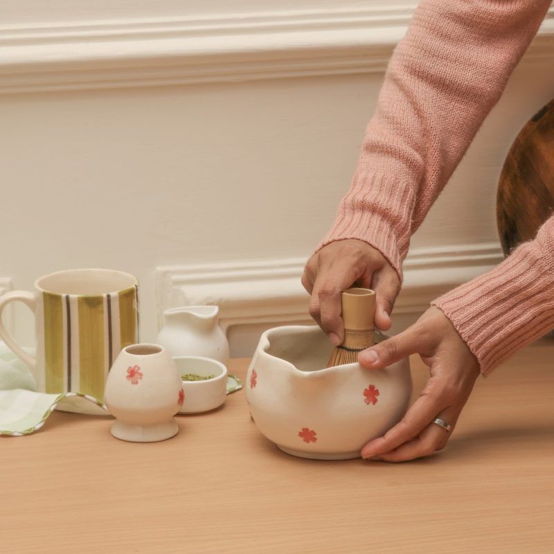 Action shot of a person whisking matcha tea in a Glimpse Homes red floral spouted bowl, highlighting the ergonomic shape and design.