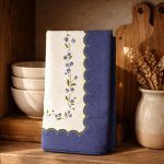 Glimpse Homes Blue Meadow Scallop Napkin folded vertically to showcase the trailing blue flower print and decorative border.