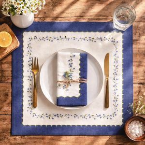 Top-down view of a Glimpse Homes Blue Meadow Scallop Napkin folded on a dinner plate, featuring a blue floral print and rustic table decor.