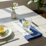 Glimpse Homes 100% cotton printed napkin with blue scalloped edges styled on a sunlit white table with a glass of water.
