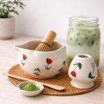 Floral bloom design ceramic matcha set by Glimpse Homes shown on a table next to a glass of iced matcha latte.