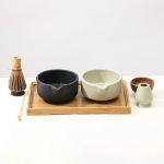 Front view of Glimpse Homes matte black and mint green ceramic matcha bowls with matching whisk holders displayed together on a wooden tray.