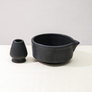 Glimpse Homes matte black ceramic set featuring a ribbed matcha bowl with pouring spout and a matching ceramic whisk holder stand on a white background.