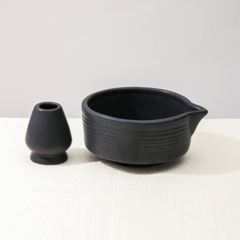 Glimpse Homes matte black ceramic set featuring a ribbed matcha bowl with pouring spout and a matching ceramic whisk holder stand on a white background.
