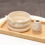 Glimpse Homes matte off-white ceramic matcha bowl and matching whisk holder stand featuring a black speckled pattern and puffy double-ring design.