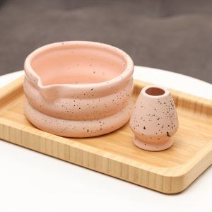 Glimpse Homes matte pink ceramic matcha bowl and matching whisk holder stand featuring a black speckled pattern and double-ring shape.