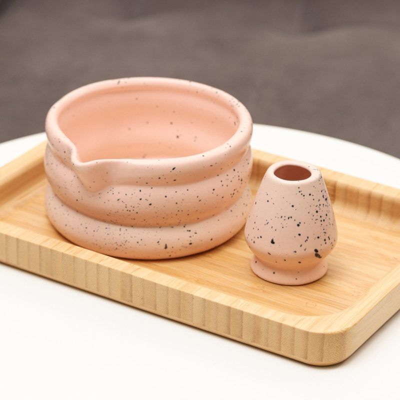 Glimpse Homes matte pink ceramic matcha bowl and matching whisk holder stand featuring a black speckled pattern and double-ring shape.