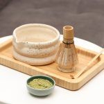 Glimpse Homes matte ivory speckled ceramic matcha bowl and whisk holder displayed on a wooden tray with a bamboo whisk and matcha powder props.