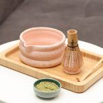Glimpse Homes matte pink speckled ceramic matcha bowl and whisk holder displayed on a wooden tray with a bamboo whisk and matcha powder props.