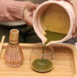 Pouring freshly whisked green tea from a Glimpse Homes matte pink spouted matcha bowl into a glass cup, showing the easy-pour spout.