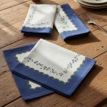 An artistic arrangement of Glimpse Homes printed cotton napkins, displaying both the folded blue scalloped edge and the full floral pattern.