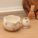 Glimpse Homes white ceramic matcha bowl with red floral design and scalloped petal rim, displayed with a matching whisk holder.