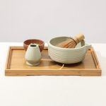 Side view of the ribbed matte mint green ceramic matcha bowl and whisk holder by Glimpse Homes arranged on a bamboo serving tray.