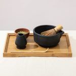 Side view of the ribbed matte black ceramic matcha bowl and whisk holder by Glimpse Homes arranged on a bamboo serving tray.