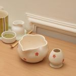 High-angle view of the Glimpse Homes petal-shaped matcha bowl with red flowers and matching ceramic whisk stand on a wooden surface.