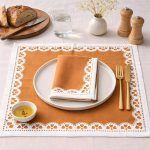 Overhead shot of a Glimpse Homes Terracotta Bloom printed cotton napkin folded on a dinner plate, styled with matching table linens.