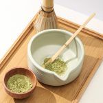 Top-down view of a Glimpse Homes matte mint green ceramic bowl containing green matcha powder and a bamboo scoop.