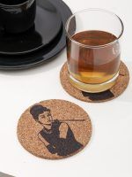 A Glimpse Homes Audrey Hepburn printed 4-inch cork coaster on a white table, paired with a glass of whiskey and black ceramic dining plates.